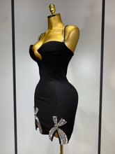 Black dress with decorative bows on a gold mannequin against a neutral background