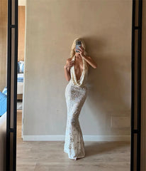 Woman taking a mirror selfie wearing a white sequin gown in a room with wooden floor and beige walls.