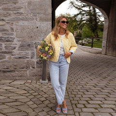 Woman in yellow jacket and light blue jeans holding flowers, standing on a stone pathway.