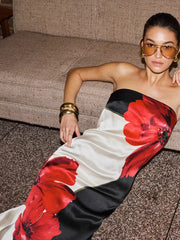 Woman wearing a strapless dress with red floral patterns sitting on a couch.