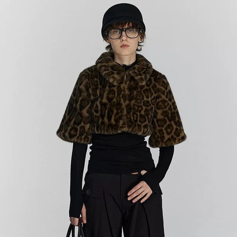 Person wearing a leopard print cape over a black outfit on a plain background