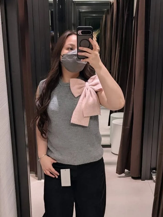 Knit vest with oversized pink bow worn by a person in a fitting room.