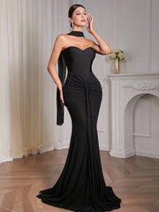 Woman in a black evening gown standing in an elegant room with a fireplace.