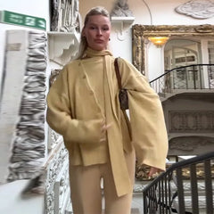 Person wearing a beige outfit standing in an elegant interior setting with decorative elements.