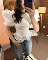 Person wearing a white blouse with ruffled details and blue jeans indoors.