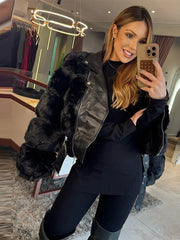 Person taking a mirror selfie wearing a black fur-lined jacket in a store.