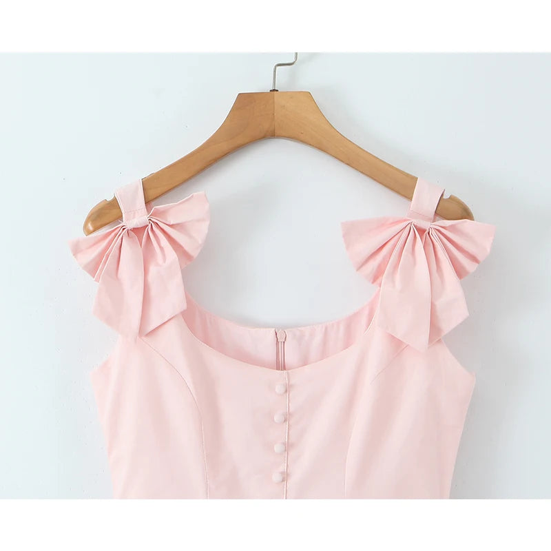 Pink top with bow shoulders on a wooden hanger against a white background