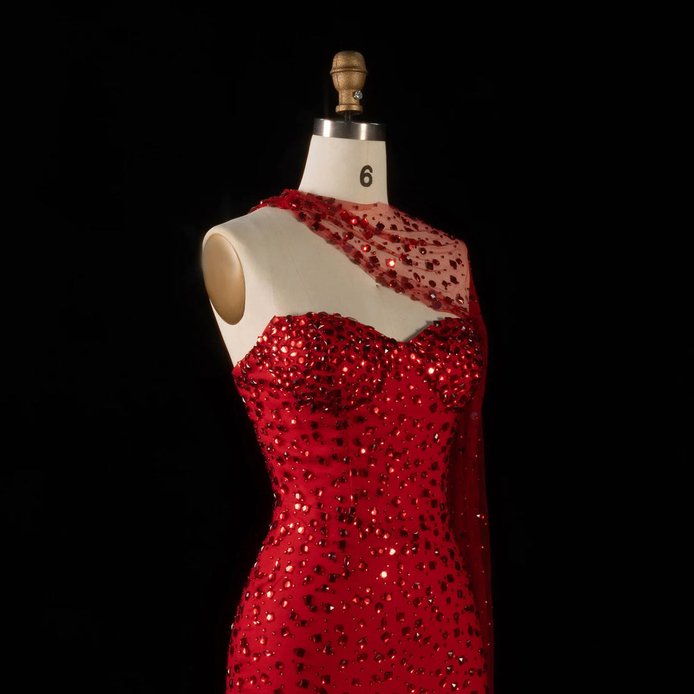 Side view of a red crystal-embellished one-shoulder trumpet gown on a mannequin.