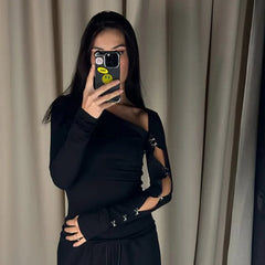 Person wearing a black outfit with cut-out design in front of beige curtains