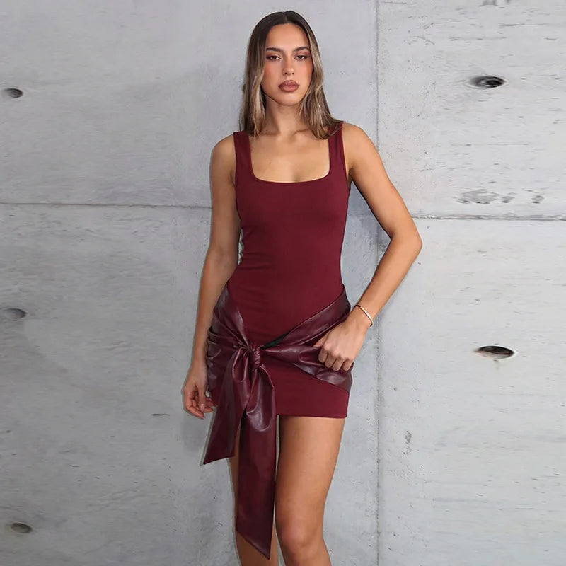 Woman wearing a burgundy dress with a large bow against a gray concrete wall.