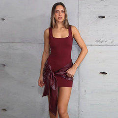 Woman wearing a burgundy dress with a large bow against a gray concrete wall.