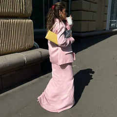 Woman in a pink outfit holding a yellow handbag and a white cup on a sidewalk.
