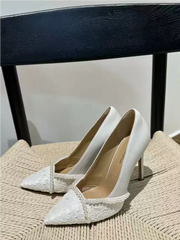 White high-heeled shoes with lace details on a textured surface.