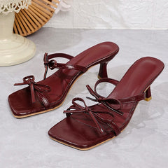 Pair of maroon high-heeled sandals with bow details on a light gray surface.