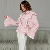 Woman wearing a pink ruffled blouse with long sleeves in a room with gray walls and a green sofa.