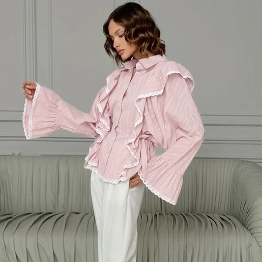 Woman wearing a pink ruffled blouse with long sleeves in a room with gray walls and a green sofa.