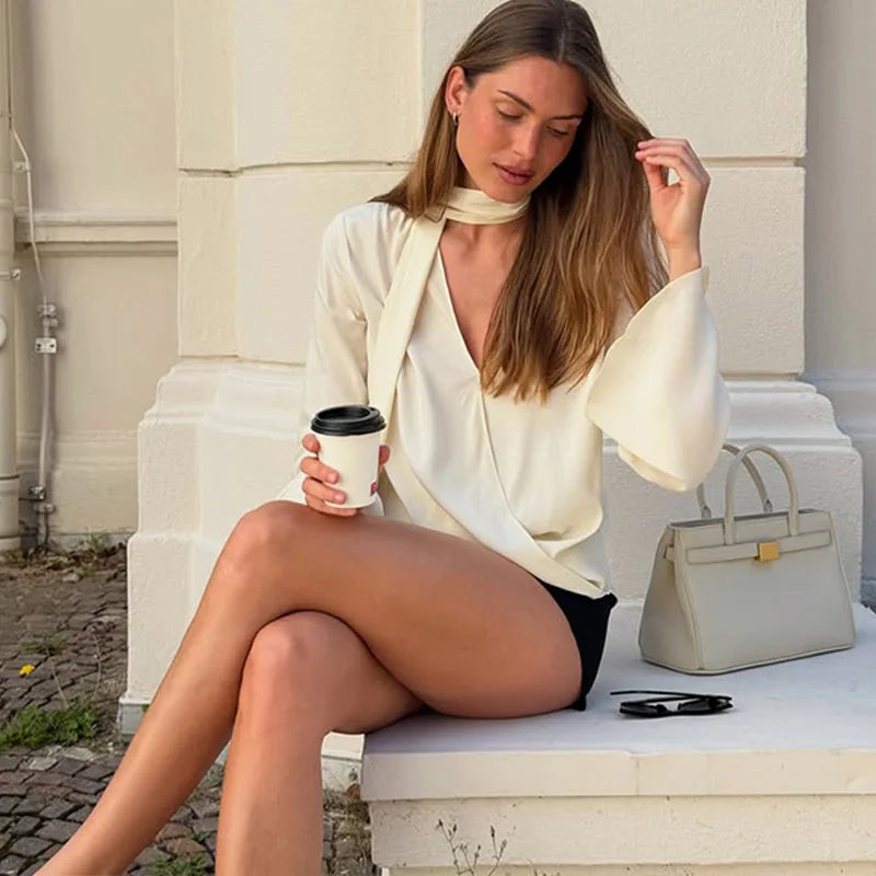 Woman sitting on steps holding a coffee cup with a handbag next to her.