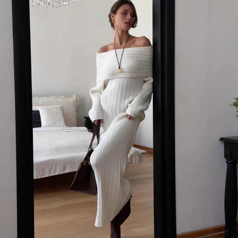 Woman in a white ribbed dress standing in a bedroom.