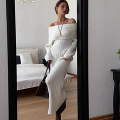 Woman in a white ribbed dress standing in a bedroom.