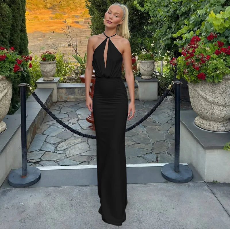 Woman in a black dress standing in an outdoor setting with plants and stone pathway.