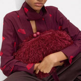 Person wearing a burgundy shirt with red heart patterns holding a textured burgundy clutch.