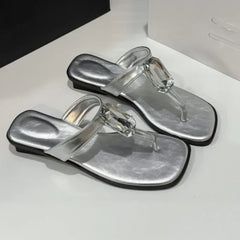 Close-up of silver square toe flat sandals with a crystal accent.
