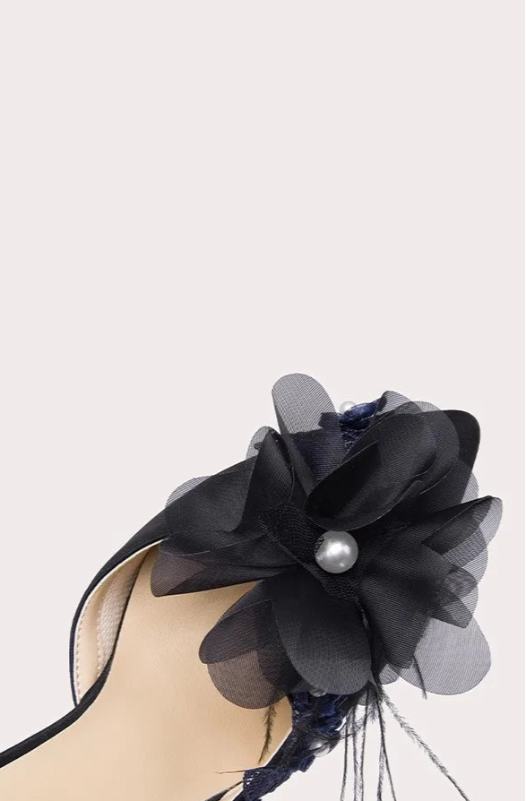 High-heeled shoe with decorative black flower on a light gray background