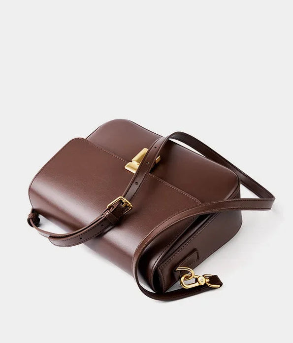 Brown leather handbag with gold accents on a light gray background