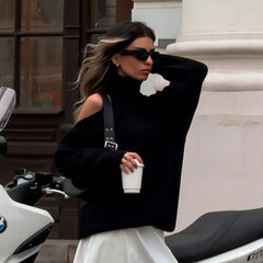 Woman in a black outfit with sunglasses and a handbag, standing next to a motorcycle.
