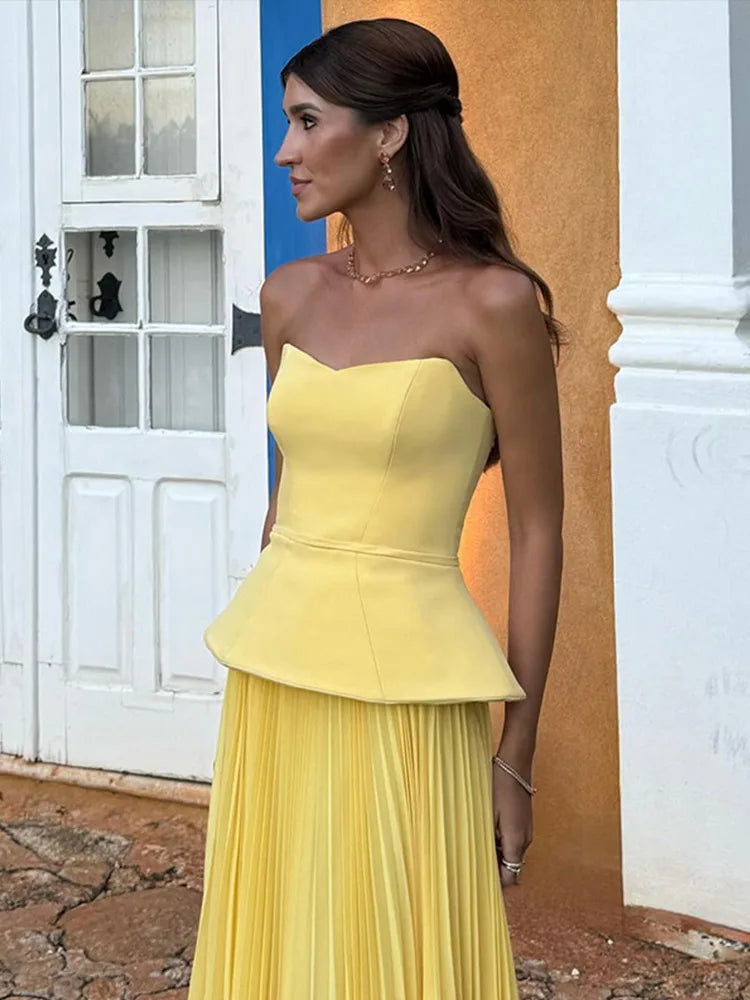 Woman wearing a yellow strapless peplum dress standing against a colorful wall.