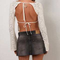Person wearing a white lace top with a brown back and a black denim skirt on a plain background