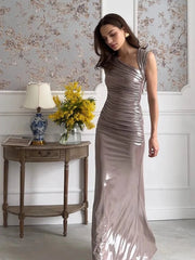 Woman in a metallic silver dress standing in a room with floral wallpaper and a side table.