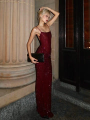 Woman in a burgundy evening gown holding a clutch, standing in front of a classical building entrance.
