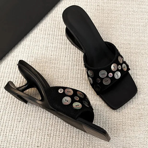 Pair of black square toe wedge heel slide sandals with decorative shell buttons.