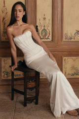 Woman in a strapless white gown sitting on a wooden chair against a decorative wall.