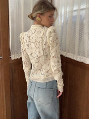 Person wearing a lace blouse and light blue jeans standing in front of a window with lace curtains.