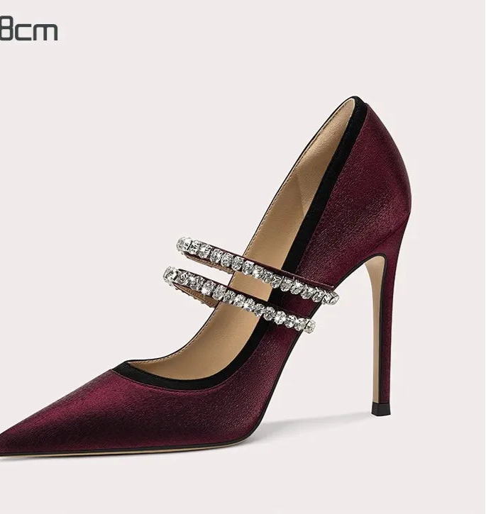 Maroon high-heeled shoe with a decorative strap on a light gray background