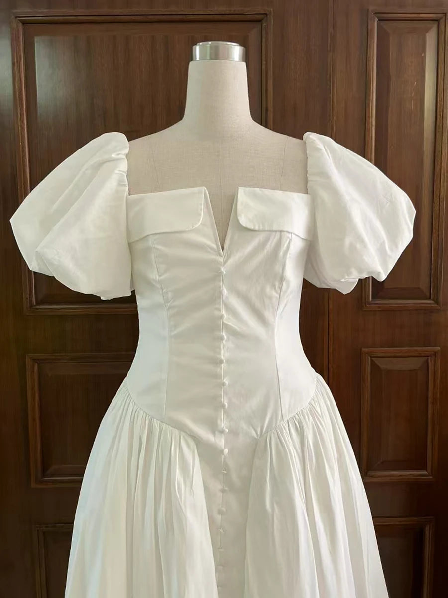 White dress with puff sleeves on a mannequin against a wooden panel background