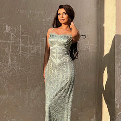 Woman in a strapless, light-colored evening gown against a textured wall.