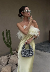 Woman in a yellow dress with feathered top holding a sequined handbag, standing in an outdoor setting with cacti.