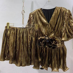 Gold pleated outfit on a hanger against a white background