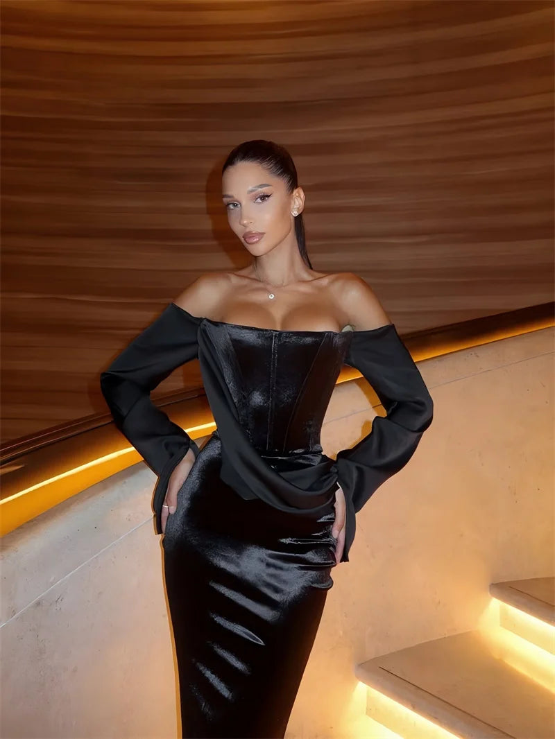 Woman wearing a black off-shoulder dress in an indoor setting with warm lighting.