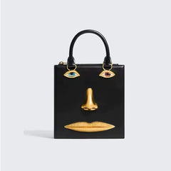 Black sculptural face embellished bag with gold-tone nose and lips, and jewel-toned eye accents.