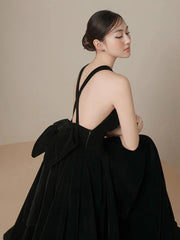 Woman wearing a black dress with a large bow at the back against a beige background