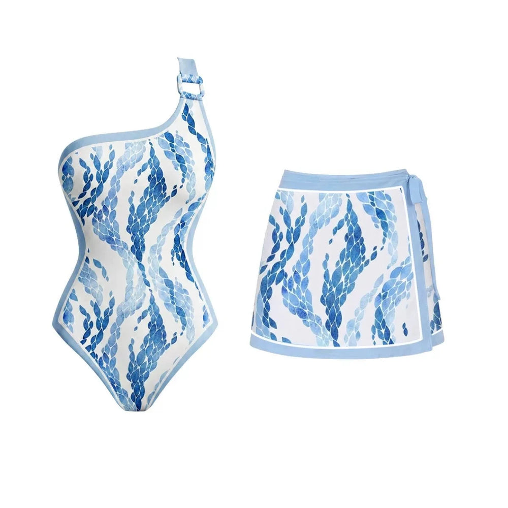One-shoulder one-piece swimsuit with blue scale print and a metal ring detail, paired with a tie-front mini skirt.