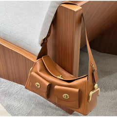 Brown PU leather shoulder bag with gold-tone hardware, displayed on a wooden chair.