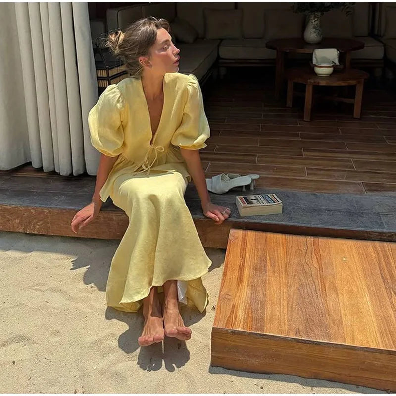 Woman in a yellow dress sitting on a wooden bench outdoors.