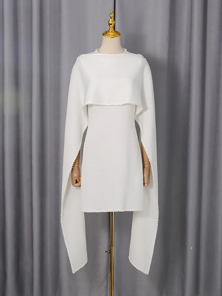 White dress with cape on a mannequin against a gray curtain background