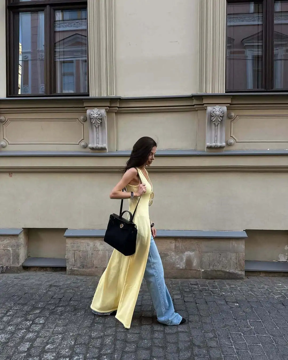 Woman in a yellow dress and blue jeans walking on a street with a building in the background