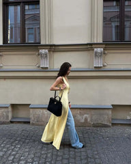 Woman in a yellow dress and blue jeans walking on a street with a building in the background